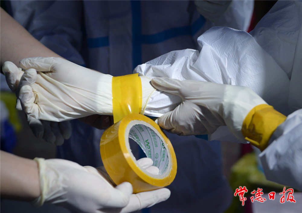 06：8月1日19時(shí)起，武陵區(qū)穿紫河街道在市體育中心設(shè)立臨時(shí)核酸采集點(diǎn)，每日6時(shí)至22時(shí)對(duì)群眾開(kāi)放。圖為醫(yī)護(hù)人員用膠帶固定手套。 本報(bào)記者 徐珊珊 攝_副本.jpg